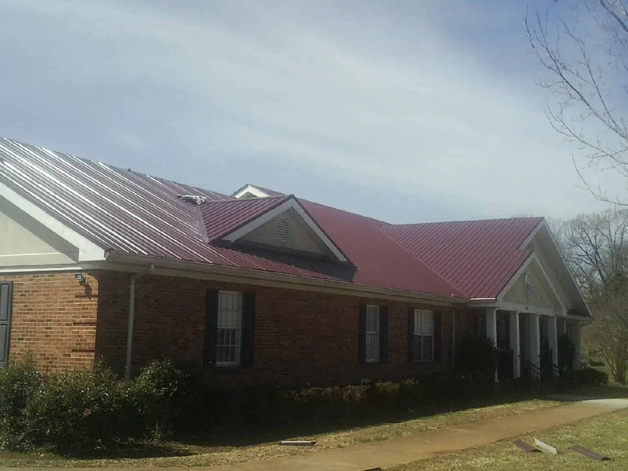 Red metal roof with gabled entries on a long brick building, from a Hail Damage Roof Repair job in Wyola