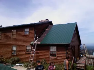 Green metal roof going on a two story log home with ladders set in Wyola
