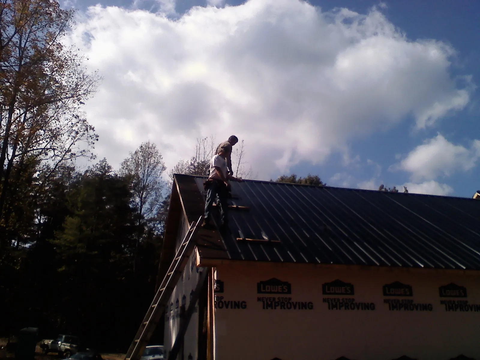 Roofer fastening dark metal panels high against a cloudy sky, from a Roof Inspection job in Wyola