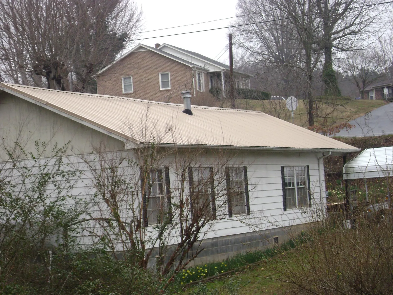 Tan metal roof on a white sided house set into a hillside — Commercial Roofing by Roofing Brothers in Wyola